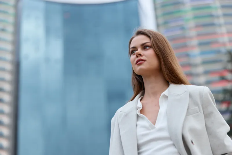 confident woman in white blazer with urban background looking upwards reflecting business ambition and success KEY: woman, confident, business, ambition, urban, blazer, success, professional, corporat