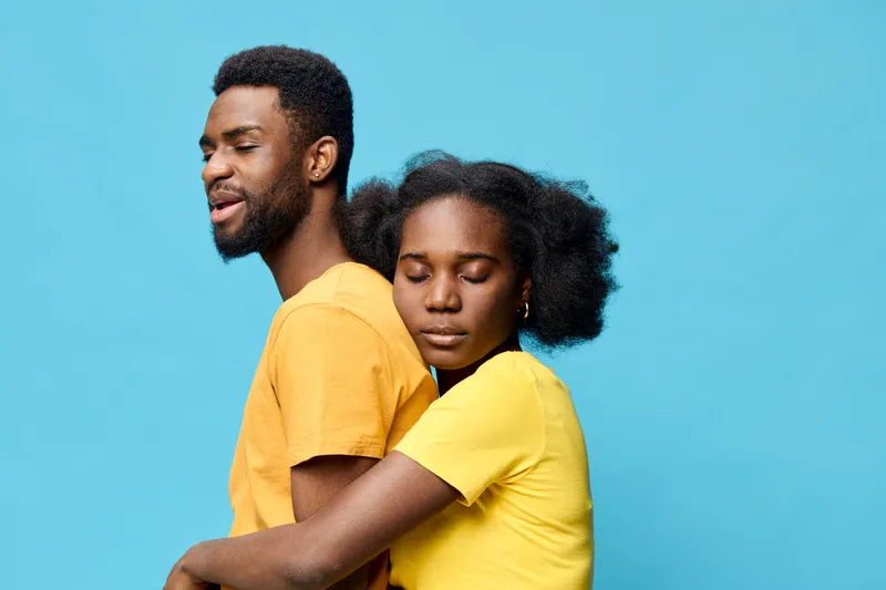 Young African couple embracing, expressing love and joy against a bright blue background, wearing matching yellow clothing that symbolizes happiness and unity