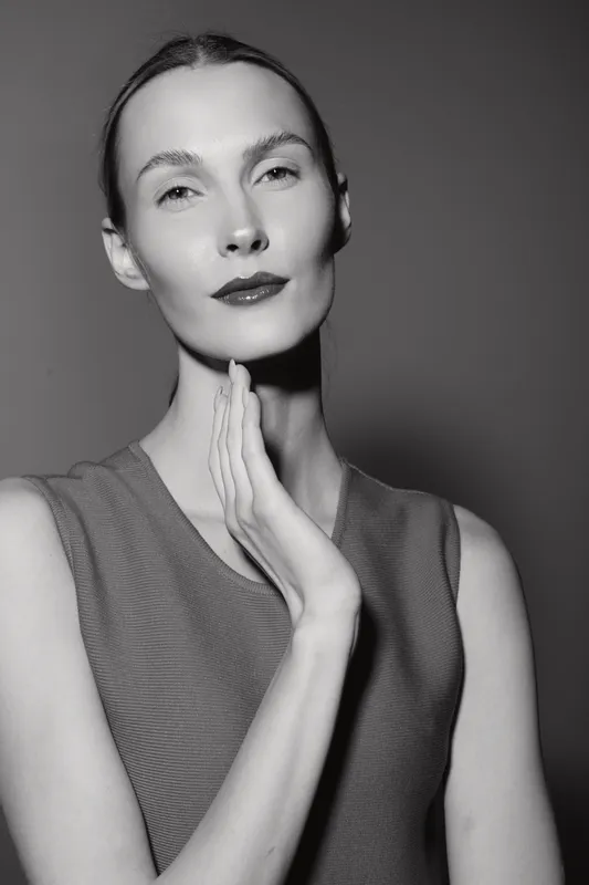 Portrait of a slim caucasian woman with fair skin and slicked back hair posing with hand on neck. Studio black and white photo with minimalistic style and elegant mood.