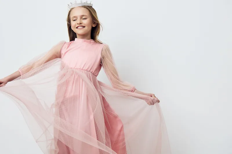 Joyful young girl in a pink dress with flowing tulle, smiling gracefully against a light background, perfect for seasonal children s fashion concepts