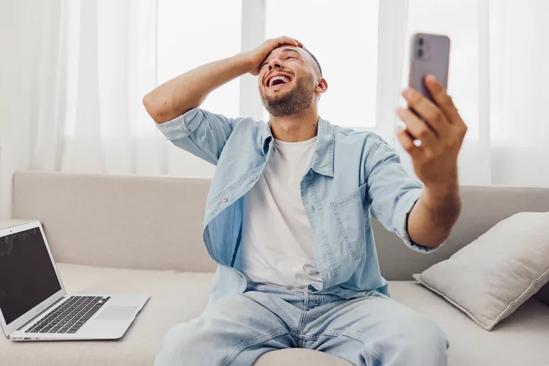 Happy man enjoying a video call at home, showcasing vibrant emotions and modern lifestyle. Perfect for social media and communication themes in 2025.
