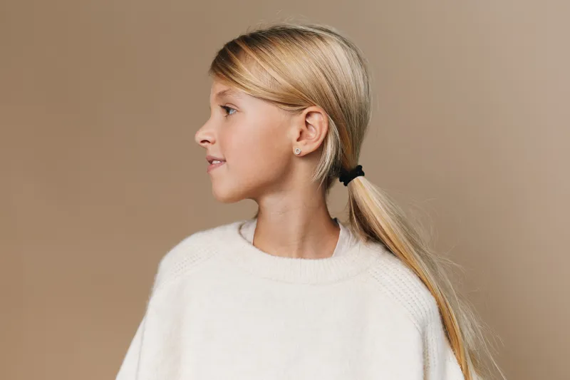 Portrait of a young woman in a soft white knit sweater, shown in profile against a warm neutral studio backdrop. serene expression, clean lines, gentle lighting enhances features.