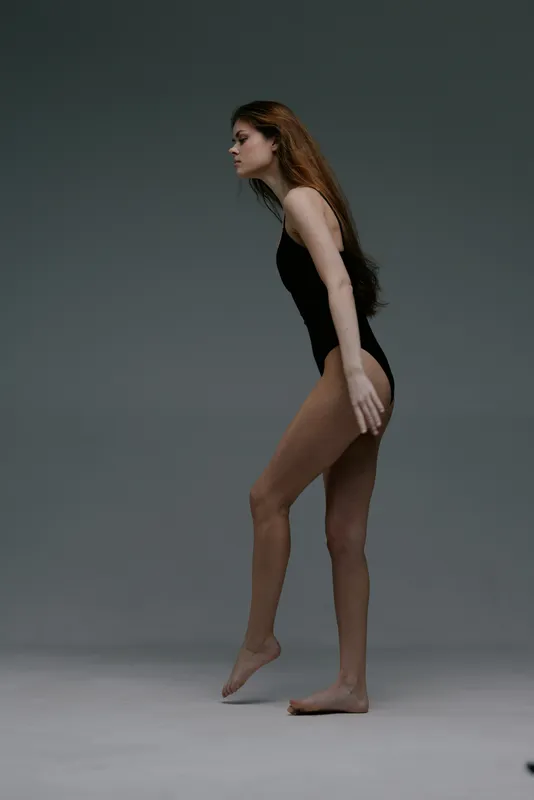 Slender woman in black bodysuit balancing gracefully against neutral gray background