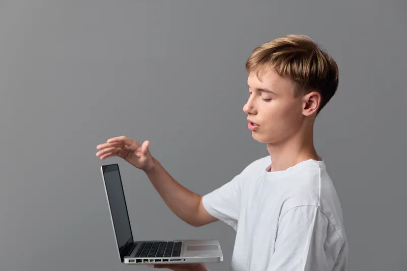 A laptop gesture by a male figure in a casual studio, emphasizing technology, education and online learning during a focused, modern workspace moment