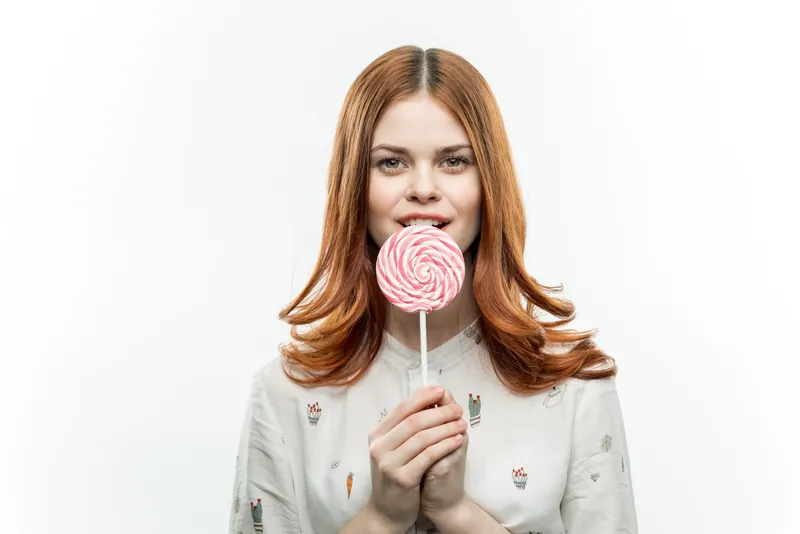 Женщина с леденцом в руках, рыжие волосы, наслаждение и веселье