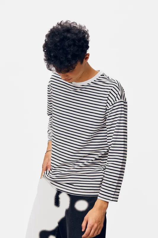 Young man wearing a striped shirt with curly hair looking down against white background, casual style, relaxed posture, modern fashion, minimalistic studio shot.