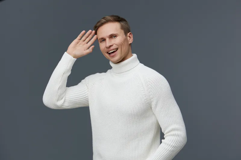 smiling man wearing white sweater waving hand gesture isolated on gray background video call digital nomad concept cheerful young caucasian person