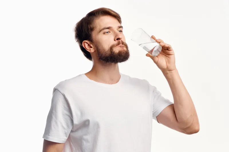 Симпатичный парень со стаканом воды на белом фоне, футболка, обрезанный вид