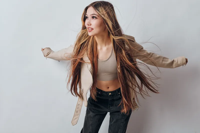 Young woman with long hair wearing casual beige jacket and crop top posing on light background with dynamic posture and confident expression in studio.