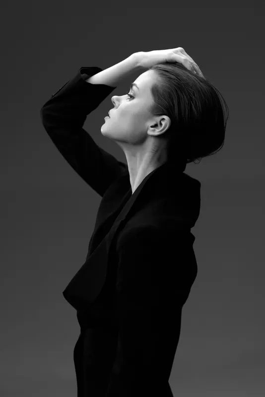 Black and white profile of a woman in a black suit with a contemplative expression and hand on head.