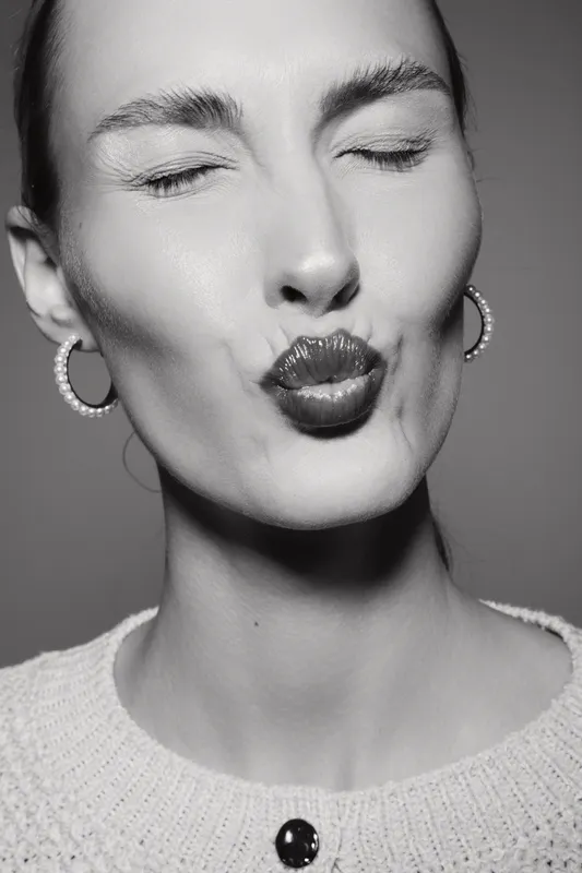Young caucasian woman with fair skin puckers lips as if giving a kiss in black and white photo.