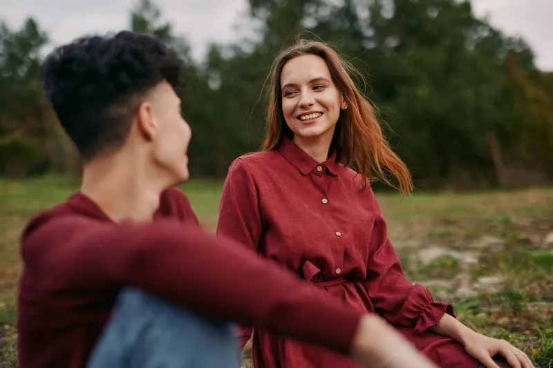 A candid scene shows a smiling woman and a man in a field, wearing casual attire, capturing authenticity through natural expressions and spontaneous interaction.