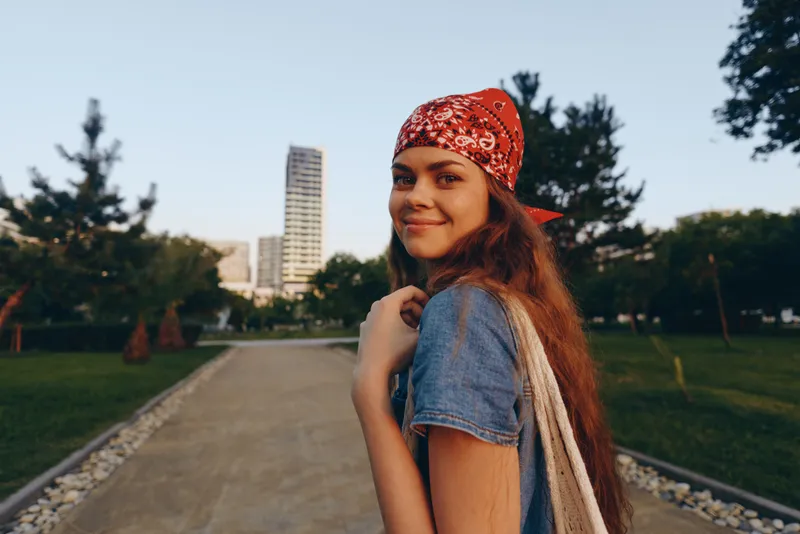 lifestyle woman in modern boho-western denim street style wearing a red bandana with natural makeup, smiling outdoors in warm film color tones