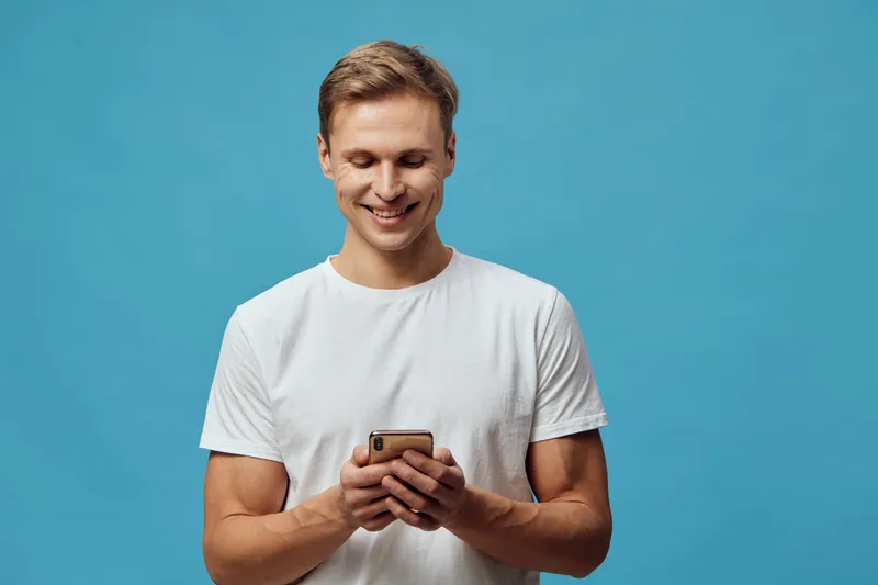Smiling young caucasian man use mobile phone chat with AI digital communication technology casual white t-shirt blue background