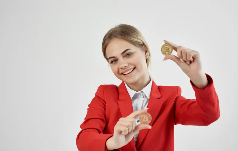 Жизнерадостная деловая женщина в красном пиджаке с криптовалютой Bitcoin и электронными деньгами