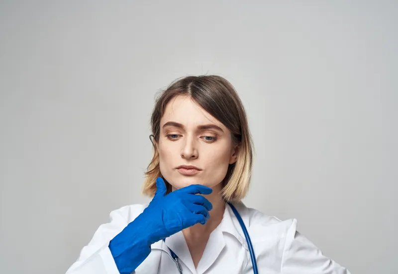 Эмоциональная женщина в синих медицинских перчатках касается головы руками на светлом фоне