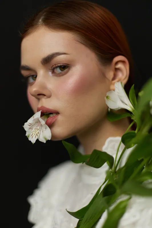 Elegant woman with white flowers in her mouth, showcasing delicate beauty on a dark background, symbolizing purity and serenity