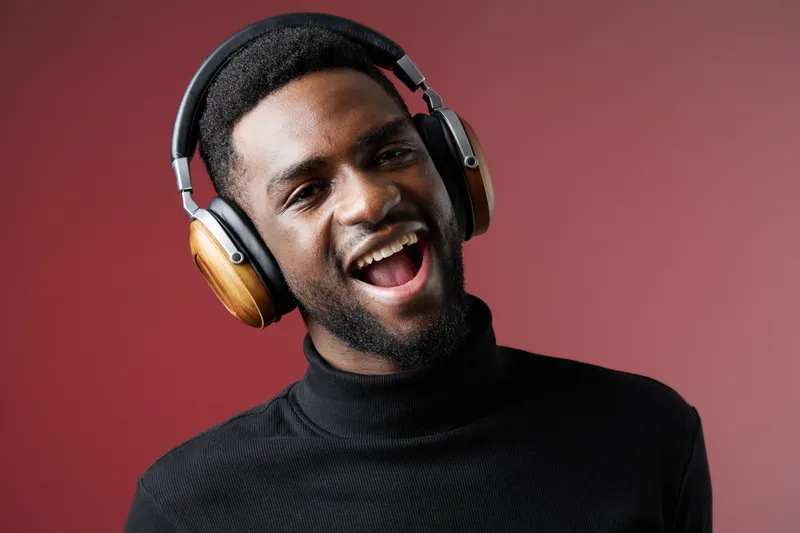 Happy young man enjoying music with headphones against a vibrant red background, showcasing a modern lifestyle and joyful emotions
