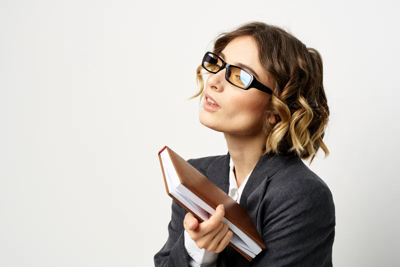 Женщина на работе с книгой в руке на светлом фоне, в классическом костюме и очках, изображение головы