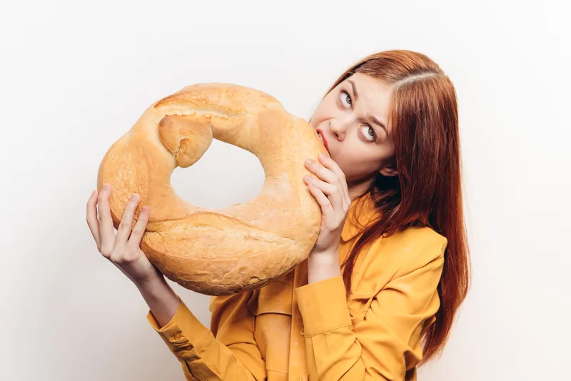 Мучной продукт, буханка хлеба и женщина в желтой рубашке на заднем плане, светлый фон, обрезанный вид