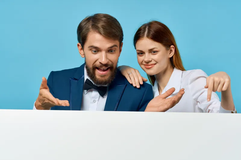 Деловой мужчина и женщина держат белый рекламный плакат-макет на синем фоне