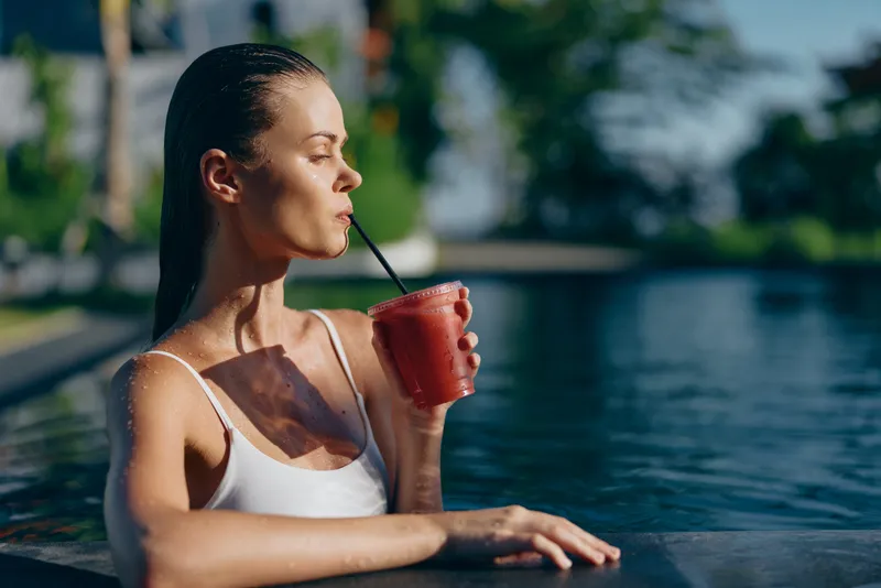 woman pool drink straw summer outdoors sunshine leisure hydration bikini poolside lifestyle relaxed moment with bright colors by water