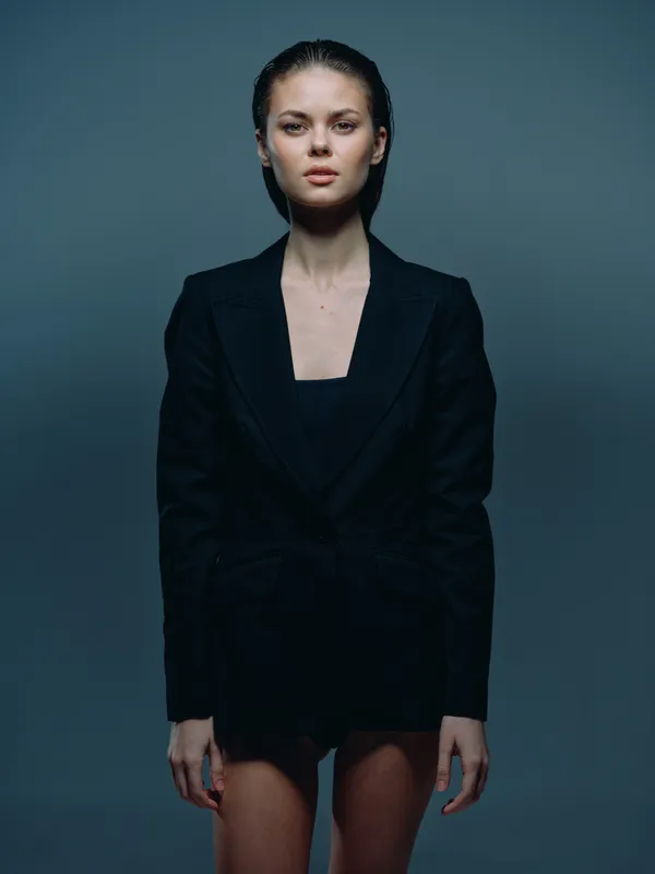 serious woman in black blazer standing with confident posture against dark background