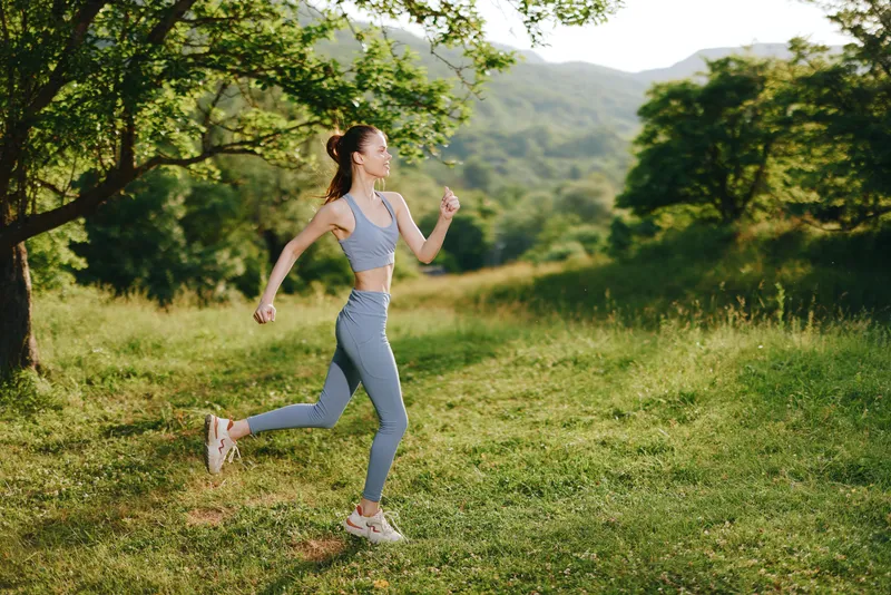 Fit young woman running in activewear in a lush green park setting, embodying healthy lifestyle and outdoor fitness motivation during summer