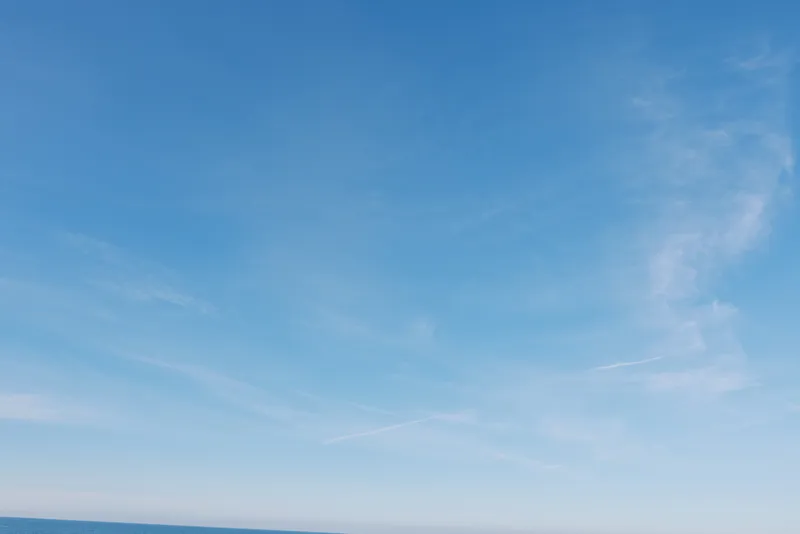 Clear blue sky over calm ocean with distant horizon and light wispy clouds, tranquil outdoor landscape ideal for travel, nature, mindfulness, relaxation visuals and serene inspiration