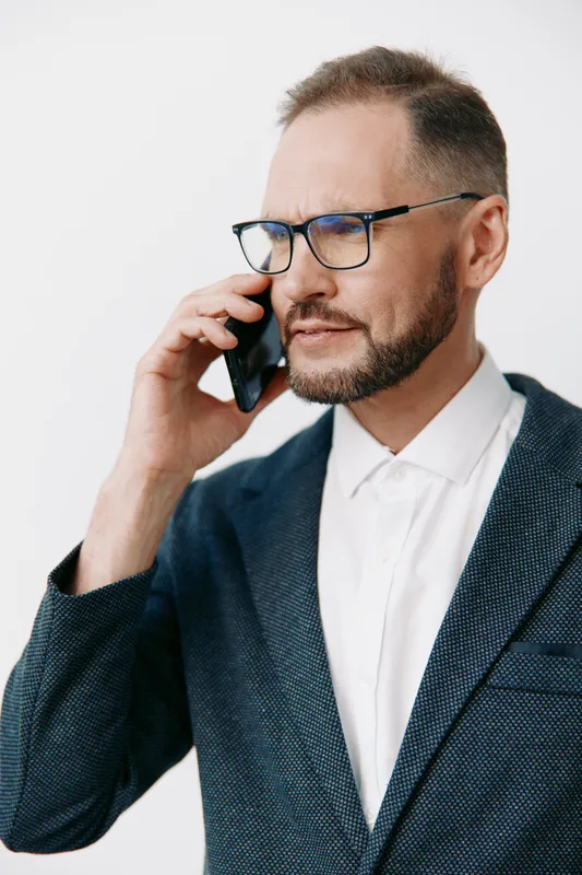 A professional man in a tailored blazer speaks on a mobile phone, conveying confidence and focus against a solid colored background. The composed expression reflects leadership.