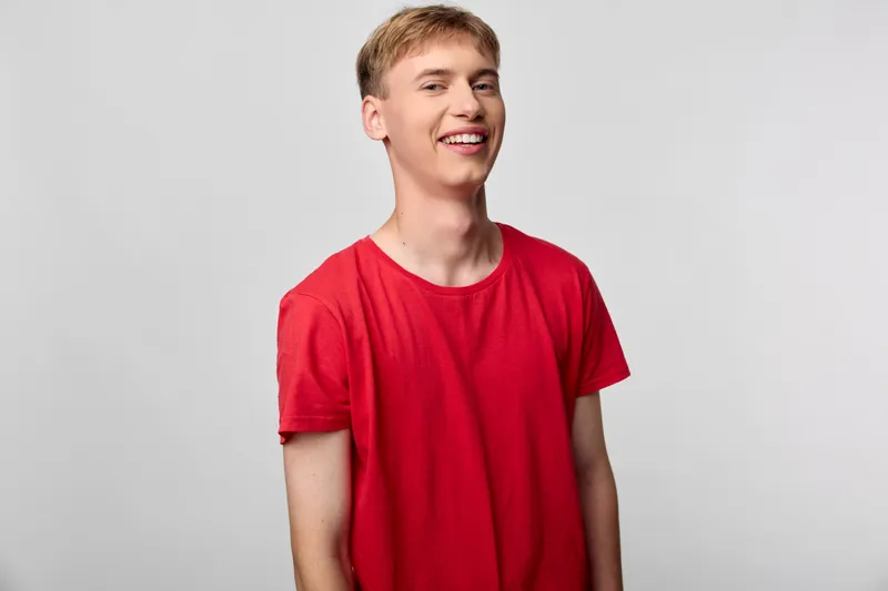 Smiling man wearing a red shirt, in a studio with neutral background, showcasing casual style, positive mood and versatile framing for branding, lifestyle, and advertising campaigns.
