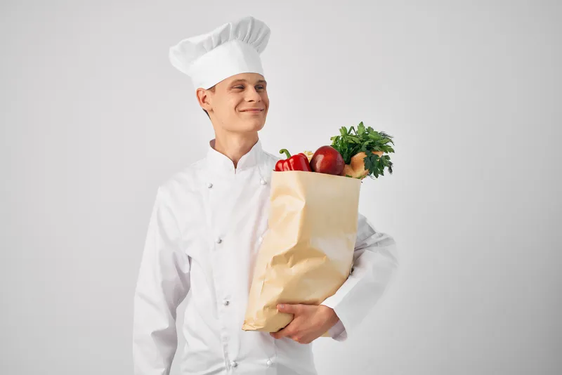 Повар с пакетом продуктов на кухне занимается приготовлением еды