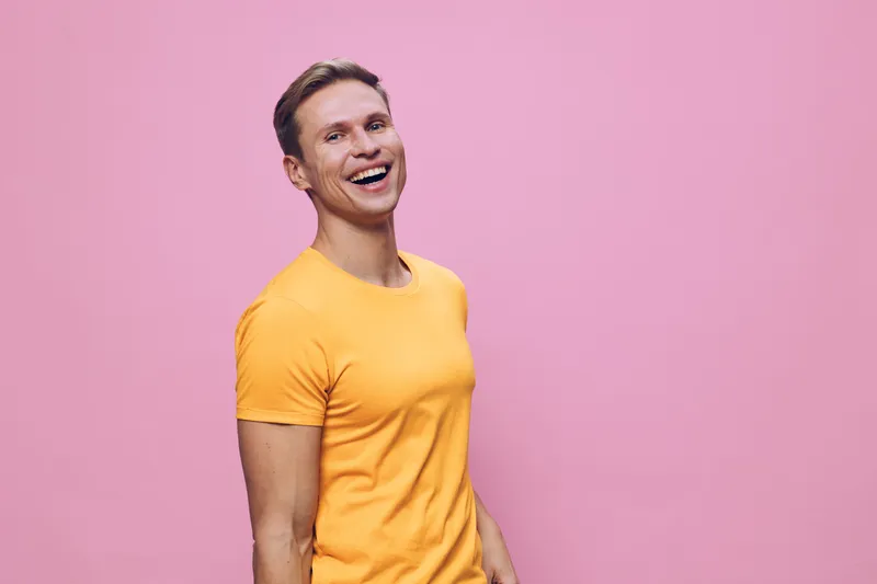 Smiling woman with short hair wearing yellow t-shirt standing against pink background, cheerful mood, casual style, vibrant colors, healthy lifestyle, studio shot.