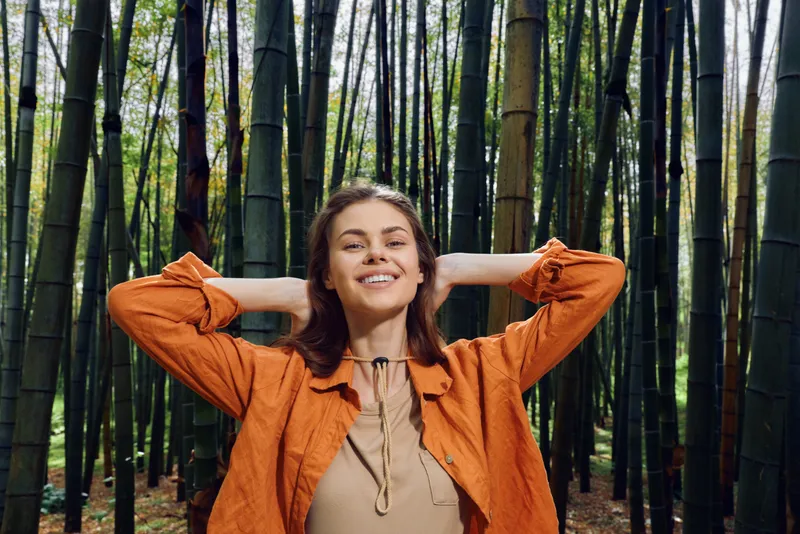 Woman smile portrait in a bamboo forest, nature scene with a relaxed young woman posing outdoors, enjoying green foliage and peaceful surroundings with confident joyful expression.
