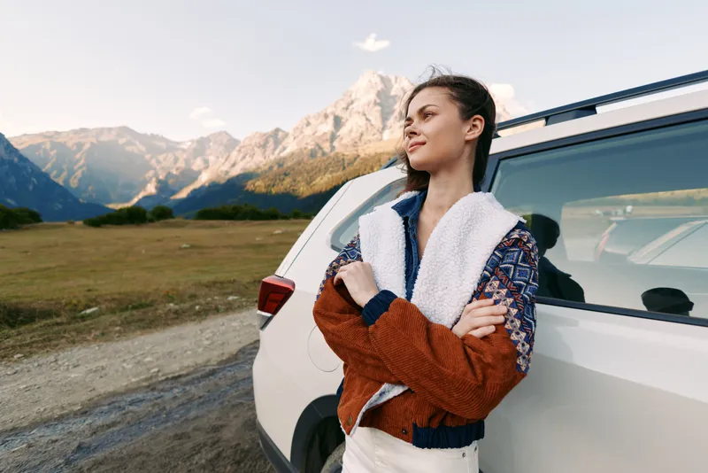 woman car mountains travel roadtrip jacket outdoors nature portrait of a young traveler leaning on SUV, scenic mountain horizon and freedom during a relaxed adventure in open landscape
