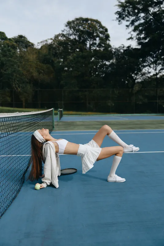 Young female tennis player in sporty outfit relaxing on court, expressing joy and confidence in a vibrant outdoor setting, capturing the essence of summer sports