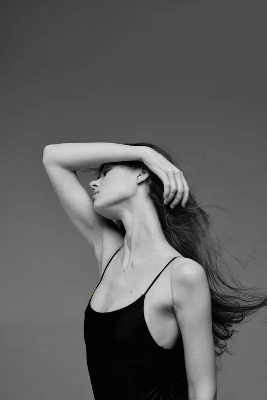 Black and white portrait of a slender woman with long hair posing gracefully against a plain background.