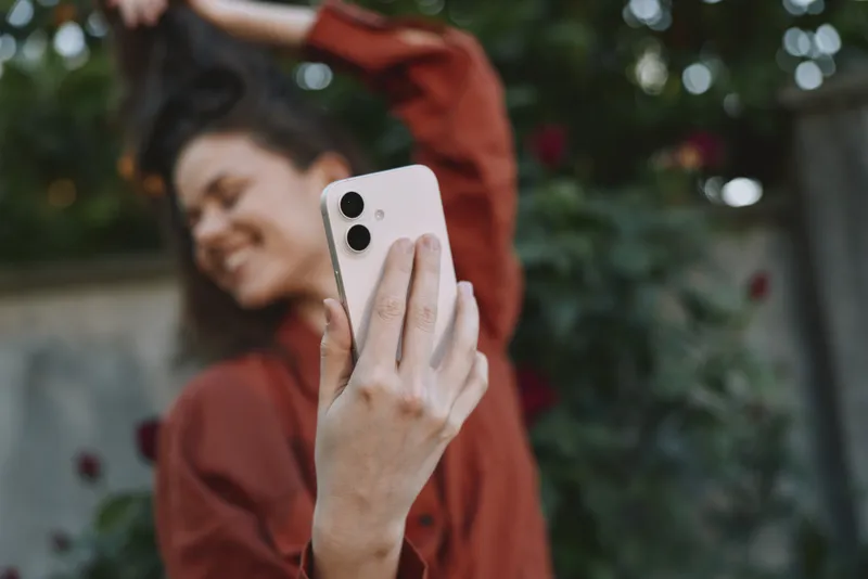 Smiling woman outdoors taking a selfie with smartphone, casual outfit, greenery in background, natural light, everyday moment, lifestyle photography, focus on selfcare and confidence, vibrant colors