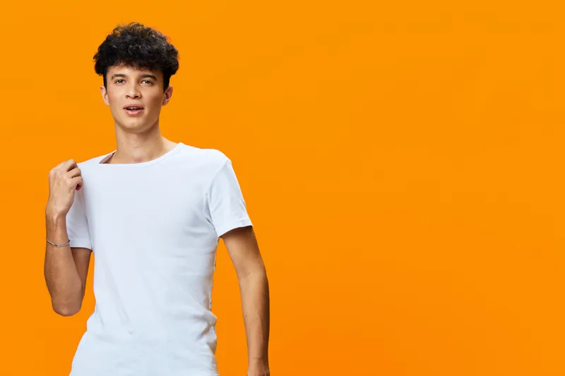 Young man in white t-shirt posing confidently against bright orange background, casual style, curly hair, relaxed expression, modern fashion.