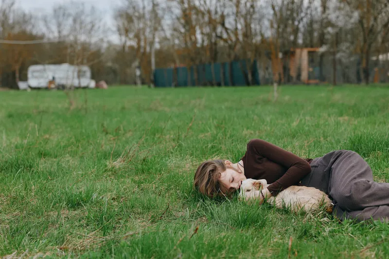 Relaxed woman lying on grassy meadow in a rural setting, sharing a gentle moment with a curious goat kid, showcasing outdoor lifestyle and calm bond with animal