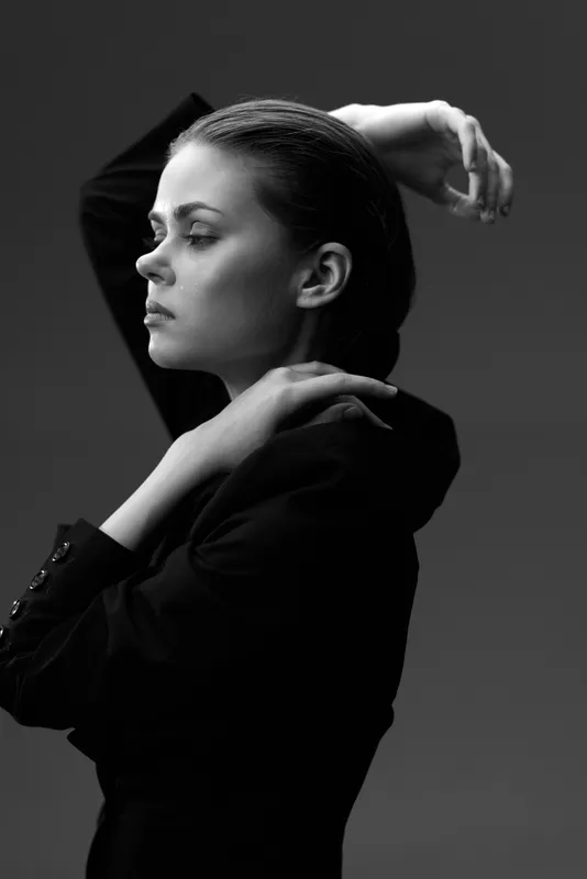 Black and white portrait of a serious woman in elegant attire with a minimalist dark background