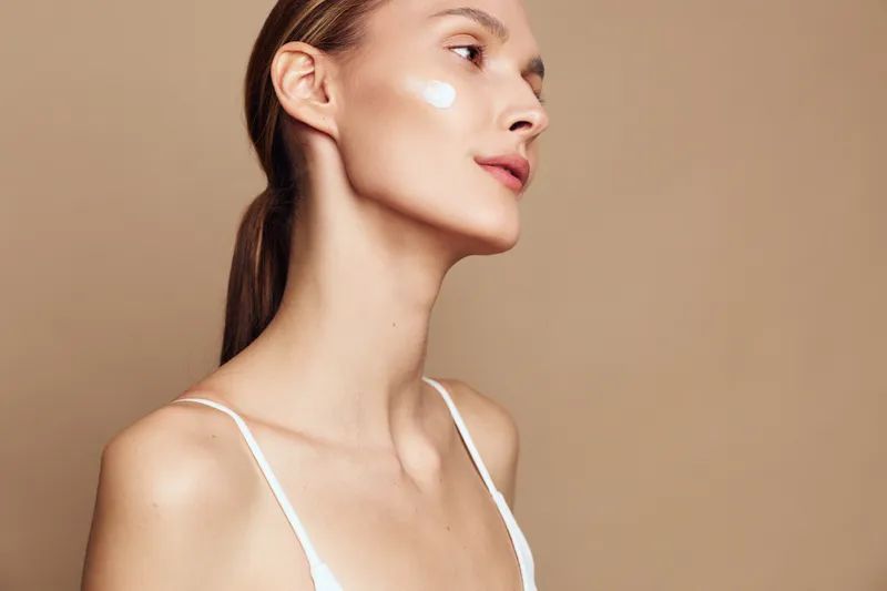 Young woman with natural skin cream on cheek, side profile, smooth complexion, soft lighting, serene expression, neutral background, beauty skincare concept