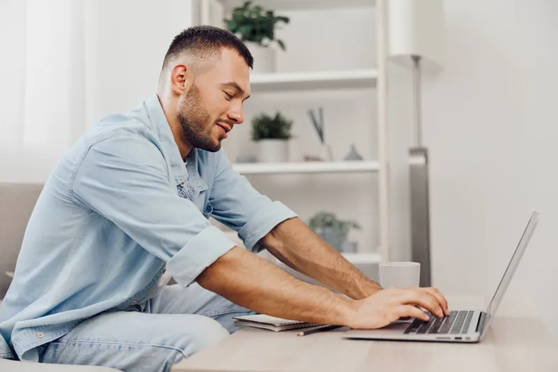 Focused man working on a laptop at home, wearing casual attire and enjoying productivity. The modern workspace is bright and inspiring, fostering creativity and motivation. ###