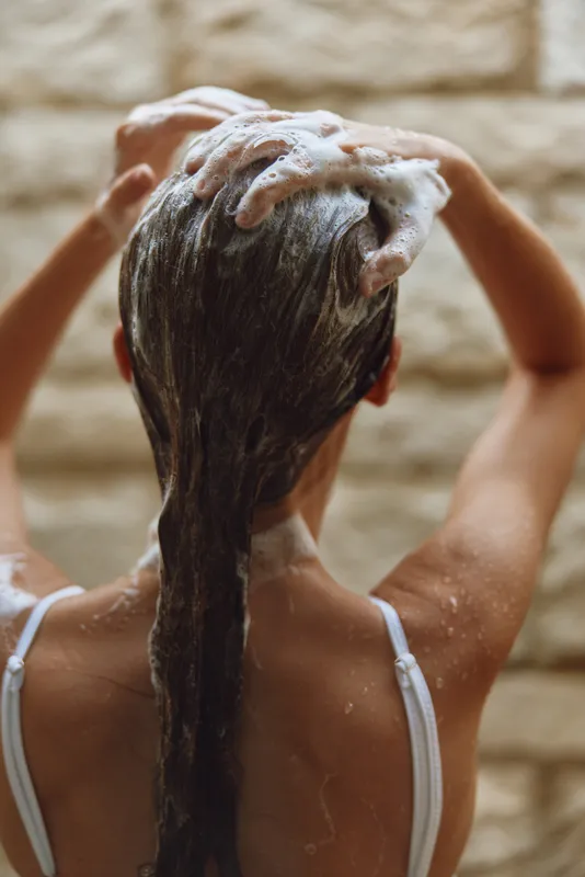 woman washing hair with shampoo foam, wet long brown hair, spa bathroom background, skincare routine, healthy hair care, natural light