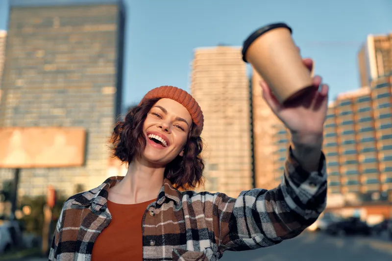 Woman smile with coffee in city street portrait at morning, candid urban moment capturing authenticity, golden hour glow and mindful living, emotional storytelling in a cozy lifestyle scene