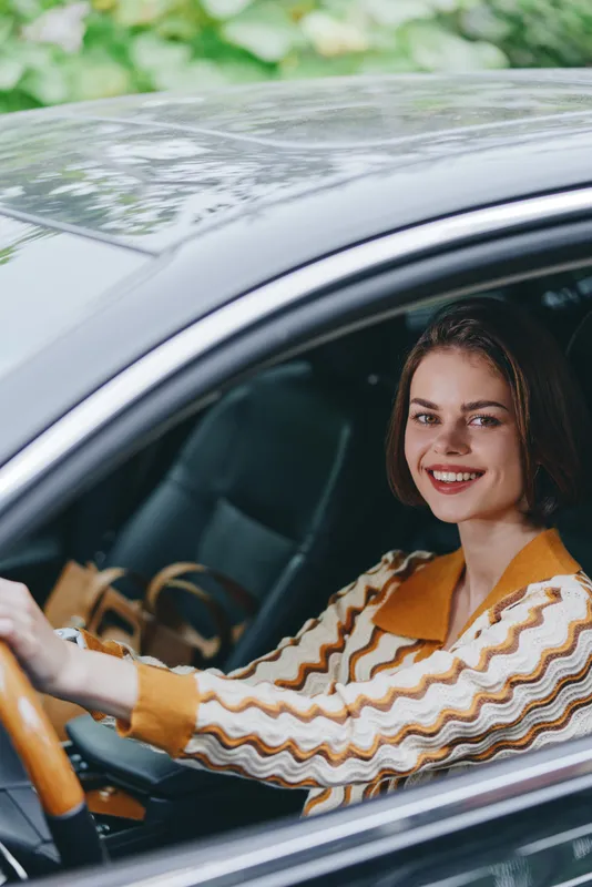Cheerful woman driver sits behind the wheel, smiling warmly at the camera, showcasing confidence, style, and a relaxed everyday commute.