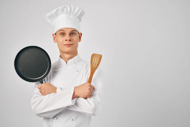 Повар с кухонной утварью, сковородой, работает и готовит