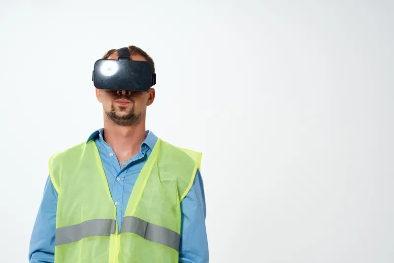 Рабочий в белой каске позирует в студии, надев VR-очки для строительства