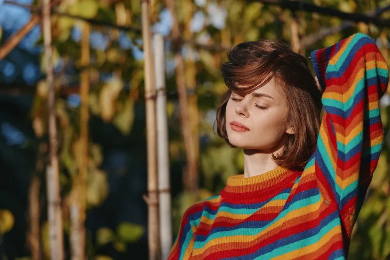 woman portrait sweater sunlight closed eyes relaxed colorful outdoor portrait of a young woman in a rainbow striped sweater basking in warm sun with serene expression