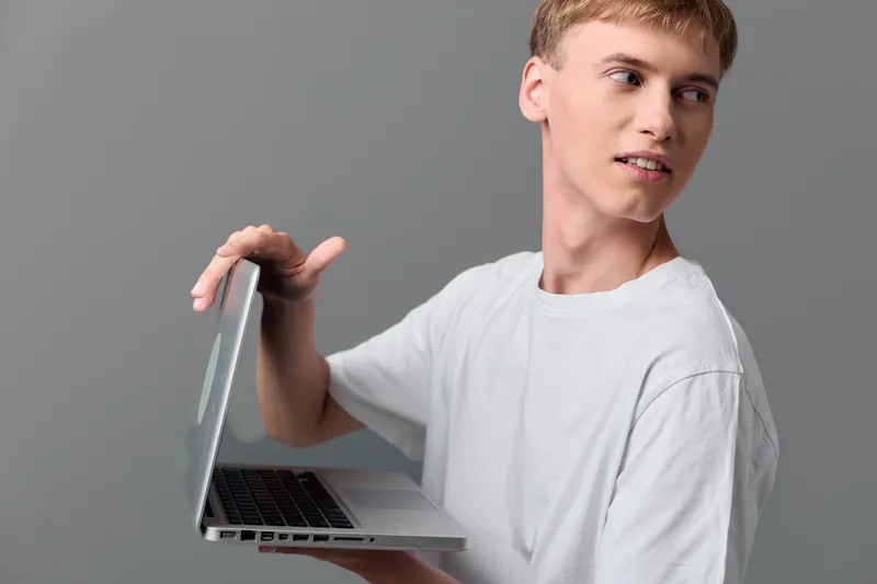 Casual young man holding a laptop in a clean studio, showcasing tech use, learning and remote work, with a neutral gray background for education and digital communication